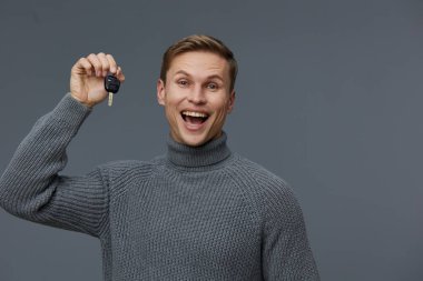 Günlük kıyafetler içindeki neşeli genç adam gri stüdyo arkaplanına gülümserken arabanın anahtarını gösteriyor. Konsept: mutluluk, yeni araba mülkiyeti, kutlama, güven, yaşam tarzı