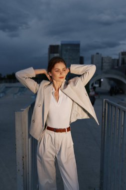 Şık bir iş elbisesi giymiş kendine güvenen bir kadın şehir ortamında poz veriyor. Büyüleyici bir silüeti ve modernliği var..