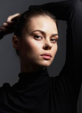 Zarafet ve özgüven sergileyen güzel bir genç kadının portresi. Saçları kasvetli, karanlık bir arka plana doğru taranmış. Moda ve modern güzelliği vurguluyor.