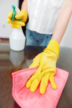 Üstünde bez parçası ve temizleme solüsyonu olan sarı eldivenli bir kadın..