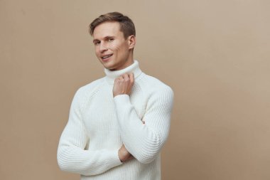 Gülümseyen adam beyaz örülü süveter giyer çapraz kol duruşu yapar kameraya bakar rahat bir şekilde bej arka plan dijital göçebe yaşam tarzı uzaktan iletişim teknolojisi mutluluğu için..