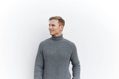 Gri örgü süveter giyen, gülümseyen, beyaz arka planda, günlük tarz ve kısa saç kesimi olan beyaz bir adam. Dijital göçebe yaşam tarzını temsil eden rahat genç adam