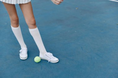 Mavi tenis kortunda spor kıyafetli bir bayan tenisçi, çeviklik ve kendine güven gösterirken aynı zamanda spor ve spor temaları için mükemmel bir tenis topuyla etkileşim içinde.