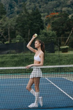 Beyaz spor giyimli enerjik bayan tenisçi güneşli bir günde hizmet etmeye hazırlanırken konsantrasyonunu gösteriyor yemyeşil arka plan aktif yaşam tarzını geliştiriyor.