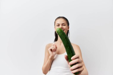 Elinde salatalık olan bir kadın beyaz arka planda seks oyuncağı taklidi yapıyor. Yüksek kalite fotoğraf