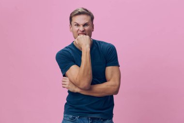 Kendine güvenen, sıradan mavi tişört ve kot giyen, kolları çapraz duran ve elleri pembe arka planda çene üzerinde duran neşeli bir adamın portresi. Yakın çekim, neşeli bir görüntü.