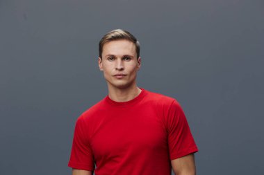 Kırmızı tişörtlü, kendine güvenen bir gencin profesyonel stüdyo portresi. Gri arka planda sakin bir ifadeyle kameraya bakıyor. İş, yaşam tarzı ya da moda temaları için mükemmel.