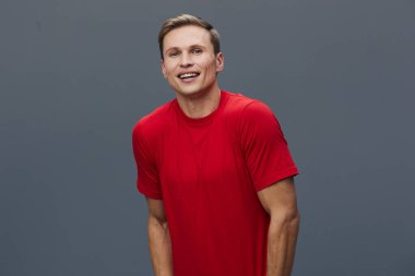 Gülümseyen genç adam kırmızı tişört giyiyor. Kameraya bak. Mutlu günlük beyaz erkek. Gri arka plan stüdyo fotoğraflarında izole edilmiş..