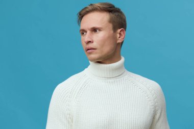 Beyaz balıkçı yaka kazak giyen, parlak mavi arka planda siber güvenlik ve dijital korumayı sembolize eden ciddi ve düşünceli bir ifadeyle yan bakan beyaz beyaz tenli bir adam.