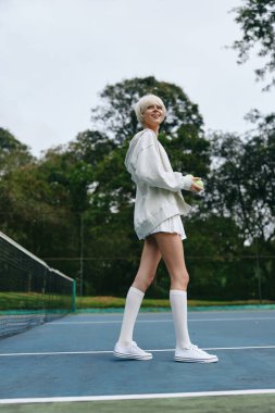 Kısa sarı saçlı enerjik genç bir kadın, spor kıyafeti giyiyor, tenis oynarken gülümsüyor enerjik yeşil arka plan spor ve neşe hissini arttırıyor, aktif yaşam tarzı için mükemmel.