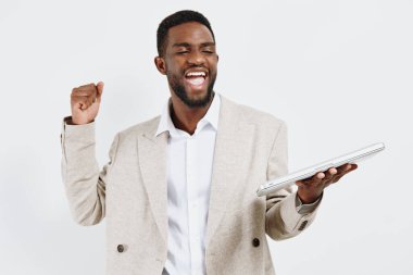 Heyecan ve başarıyı ifade eden mutlu bir adam, şık giyinmiş, tablet cihazını tutuyor, boş beyaz bir arkaplanda duruyor, coşku ve başarı gösteriyor. Konsept: Profesyonel