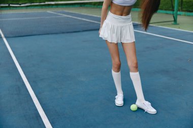 Beyaz şık bir spor kıyafeti giymiş bayan bir tenisçi, spor için zindelik ve tutkuyu vurgulayarak, bir tenis kortunda güvenle durur.