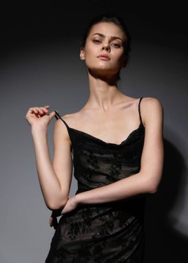 Saf siyah bir elbise içinde zarif bir manken, minimalist karanlık bir ortamda duruş ve zarafet sergiliyor. Moda, entelektüellik ve güzelliği vurgular.