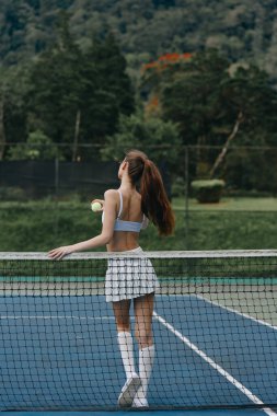 Şık kıyafetli aktif bayan tenisçi canlı bir mavi kortta güneşli bir öğleden sonranın tadını çıkarıyor, vücut bulmuş spor ve açık hava sporları.