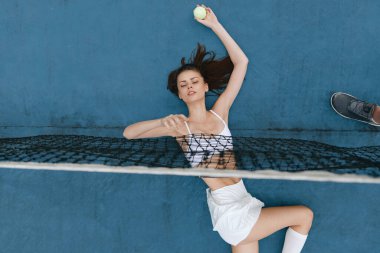 Enerjik, genç bir kadın spor kıyafetiyle canlı bir mavi kortta tenis topuna vurmaya hazırlanıyor. Kendine güveni tam ve oyununa odaklanmış.