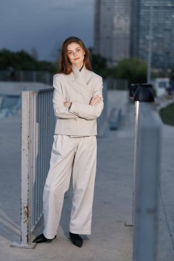 Açık gri takım elbiseli dengeli bir kadın, şehir ortamında güvenle duruyor, profesyonelliği ve iş temaları için çağdaş tarz ideallerini sergiliyor..
