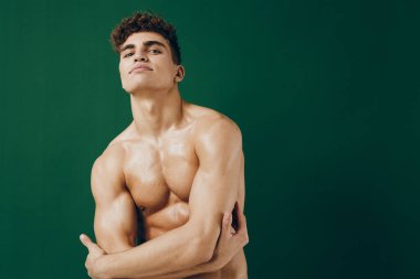 Atletik adam kendine güveni olan çapraz kollu, parlak tenli ve güçlü yapılı biri. Yeşil zemin zindeliği ve kişisel gücü vurguluyor.