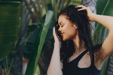 Saçları ıslak bir kadın, elleri başının üstünde palmiye ağacının önünde duruyor, tropik tatil konsepti.