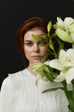 Bu portre, beyaz bir bluz giymiş, kırmızı kahverengi saçlı, beyaz zambaklar tutan genç bir kadını yakalıyor.