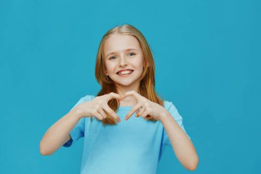Mavi gömlekli mutlu çocuk elleriyle bir kalp oluşturuyor, canlı bir mavi arkaplan karşısında duruyor, sevgi ve mutluluğu simgeliyor sağlık, aile ve mutluluk kavramları için ideal.