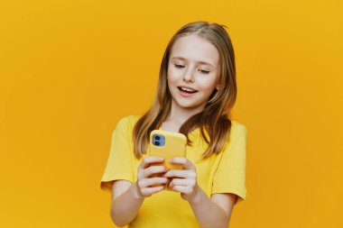 Sarı tişörtlü neşeli kız, sarı çantasıyla akıllı telefonunu kullanırken gülümsüyor, canlı sarı bir zemin üzerine kurulmuş, gençlik neşesi ve modern teknolojinin özünü yakalıyor.