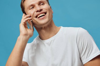 Nişanlı bir adam telefonda eğleniyor, rahat bir tarzda, parlak bir gülümsemesi olan genç bir erkek, samimi bir an, canlı mavi bir stüdyo geçmişi, pozitif iletişim ve sosyal etkileşimler.