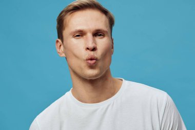 Canlı mavi bir arka planda açık kahverengi saçlı, beyaz tişört giyen neşeli bir gencin portresi, neşeli ve anlamlı bir ruh hali sergiliyor, yaşam tarzı, sosyal medya veya