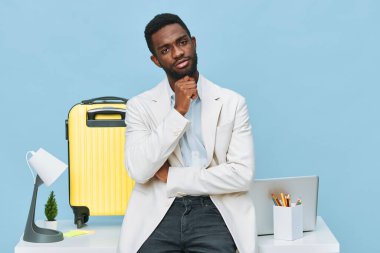 Sıradan iş kıyafetleri içinde şık bir adam, parlak stüdyo ortamında dizüstü bilgisayar ve bavulla poz veriyor, derin düşüncelere dalmış, iş seyahatine ya da iş seyahatine hazır olduğunu gösteriyor. Kavram: Profesyonel yolculuk