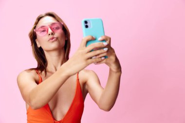 Mayo giymiş moda bir kadın, canlı pembe arka plana karşı akıllı telefon kullanarak selfie çekiyor.