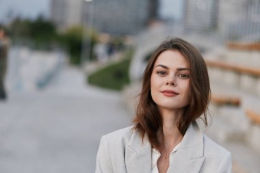 Açık gri ceketli, kentin arka planında gülen, gülen, güz modası tarzında, kendine güveni tam bir kadın.