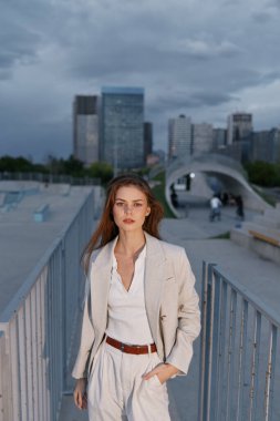 Özel dikim bir iş elbisesi içindeki şık bir kadın şehir ortamında kendine güvenerek poz veriyor. Çağdaş şehir silüetine sahip profesyonellik ve entelektüellik yayıyor..