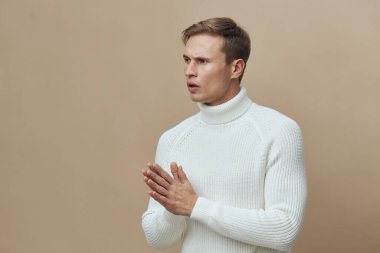 Beyaz kazaklı düşünceli bir adam, bej arka planda duran kafası karışık ya da endişeli görünüyor. Stüdyo onun yüz ifadesini ve vücut dilini görüntüler, tefekkür eder ve