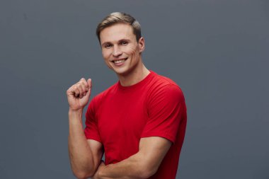 Canlı kırmızı tişörtlü neşeli bir adam, gri arka planda rahat bir pozda kameraya bakıyor. Kavram: pozitif duygu, günlük yaşam