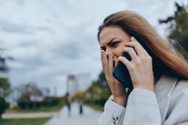 Genç bir iş kadını, şehir parkında telefonda modern iş hayatının zorluklarını somutlaştırırken kaygılarını dile getiriyor. Sahnede kentsel profesyonellik ve duygusallık sergileniyor.