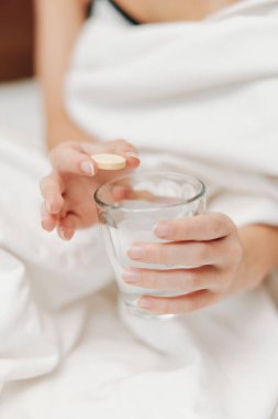 Yatakta bir bardak su ve hapla, beyaz çarşafla kaplanmış bir kadın. tedavi ve dinlenme kavramı.