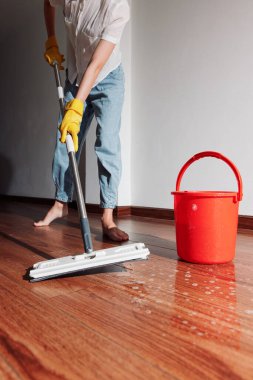 Pencerenin önündeki ahşap zemini bir kova suyla silen kadın. temizlik kavramı.