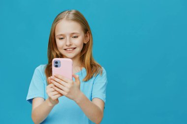 Açık mavi tişörtlü neşeli bir kız, akıllı telefonuyla meşgul, mutluluk ve modern iletişimi yansıtan canlı mavi arka plan, canlı atmosferi arttırır, kavramları için ideal.