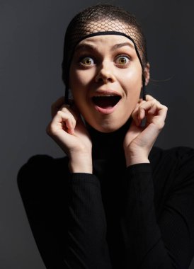 Hevesli bir kadın model, siyah bir elbise giyiyor ve balık ağıyla başını örtüyor, neşe dolu bir ifade sergiliyor. Moda ve duygu temaları için ideal.