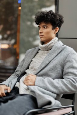 Moda genç adam gri kazak siyah kot koltuk önünde oturan yan yana bakan