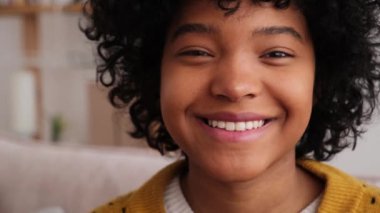Beautiful african american girl with afro hairstyle smiling sitting on sofa at home indoor. Young african woman with curly hair laughing. Freedom happiness carefree happy people concept