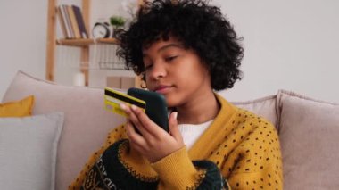 African american woman shopping online holding smartphone paying with gold credit card. Girl sitting at home buying on Internet enter credit card details. Online shopping ecommerce delivery service