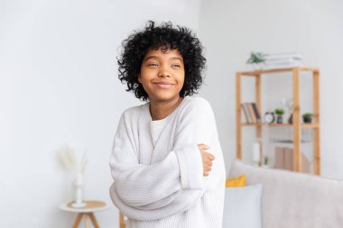 Beautiful african american girl with afro hairstyle smiling at home indoor. Young african woman with curly hair laughing in living room. Freedom happiness carefree happy people concept