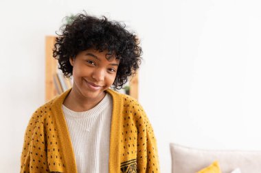 Beautiful african american girl with afro hairstyle smiling at home indoor. Young african woman with curly hair laughing in living room. Freedom happiness carefree happy people concept