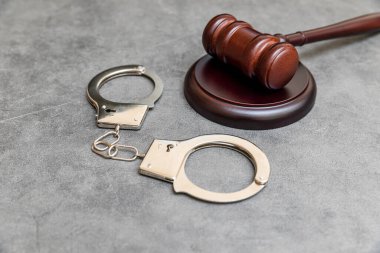Law theme. Court of law trial in session. Judge gavel handcuffs on grey table in lawyer office or court session. Mallet of judge on concrete stone grey background. Justice human rights concept