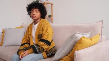 African american sad thoughtful pensive unmotivated girl sitting on sofa at home indoor. Young african woman ponder look tired after long day. Girl feels depressed offended lonely upset heartbreak