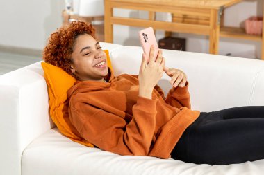 African american girl lying on couch with smartphone having video chat. Female blogger chatting with best friends in social network. Young woman having virtual meeting online chat video call at home