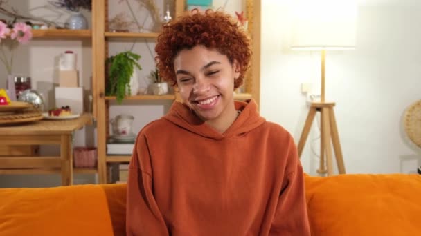 美丽的非洲裔美国女孩 有着非洲式的笑容 坐在家里的沙发上 年轻的非洲女人 卷发笑着 自由快乐无忧无虑的快乐人的概念 — 图库视频影像