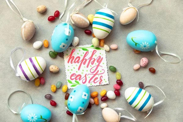 Happy Easter concept. Preparation for holiday. Easter eggs Inscription HAPPY EASTER letters candy chocolate eggs and jellybean sweets on concrete stone grey background. Flat lay top view copy space