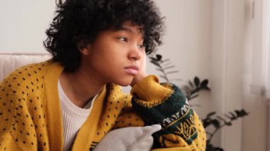 African american sad thoughtful pensive unmotivated girl sitting on sofa at home indoor. Young african woman ponder look tired after long day. Girl feels depressed offended lonely upset heartbreak