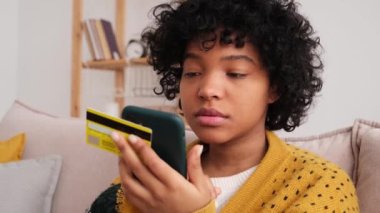 İnternetten alışveriş yapan Afrikalı Amerikalı bir kadın elinde akıllı telefonuyla altın kredi kartıyla ödeme yapıyor. Evde oturup internetten alışveriş yapan kız kredi kartı bilgilerini gir. Çevrimiçi alışveriş ekommerce dağıtım servisi